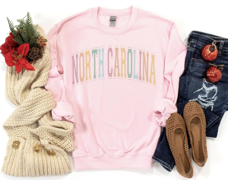 Puede incluir: Sudadera rosa de manga larga con el texto "NORTH CAROLINA" en colores arco&iacute;ris.