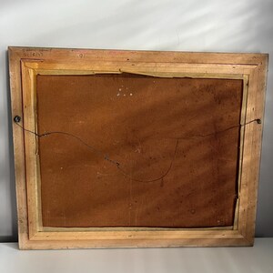 May include: Back of a framed artwork with a light brown wooden frame. The artwork's backing is a dark brown color. The frame has a wire for hanging. The upper left corner has handwritten text that reads "S. Frank-Waltz 2/16/17".