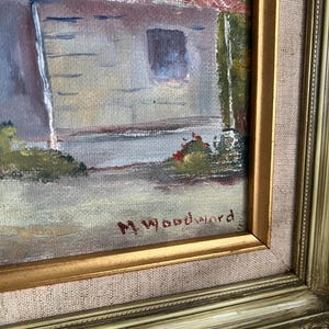 May include: An oil painting of a building with a red roof and a window, set in a landscape. The painting is signed "M. Woodward" in the lower right corner and framed in a gold-colored frame.