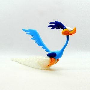 Könnte beinhalten: Eine blaue, orange und weiße Road Runner-Figur mit ausgebreiteten Flügeln und einem langen, cremefarbenen Schwanz. Die Zeichentrickfigur befindet sich in einer Laufpose, mit einem detaillierten Schnabel und ausdrucksstarken Augen.