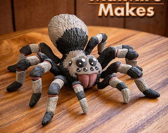 Peut inclure: Figurine d'araignée artisanale avec un corps noir et blanc, des pattes rayées et une langue rose. Le texte "MatMire Makes" est affiché en haut à droite. Le design est très détaillé.