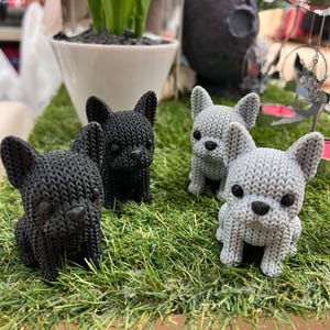 Könnte beinhalten: Vier kleine Französische Bulldoggen-Figuren mit einer strukturierten, strickähnlichen Oberfläche. Zwei der Figuren sind einfarbig schwarz und zwei sind hellgrau. Jeder Hund hat aufrechte Ohren, eine kurze Schnauze und dunkle, runde Augen.