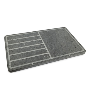 May include: A grey rectangular stone slab with a textured surface and a grid pattern carved into it. The slab is designed for use as a chopping board or trivet.