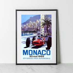 May include: Framed vintage poster of the Monaco Grand Prix 1965. The poster features a red race car speeding along a coastal road, with a cityscape and palm trees in the background. The text "MONACO" is prominently displayed in blue.