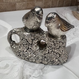May include: Silver salt and pepper shakers shaped like birds perched on a tree branch with grapevine details.