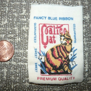 May include: A vintage calico cat brand cat food bag with a blue ribbon and the text "Fancy Blue Ribbon Guaranteed Sweet Sweet Guaranteed Premium Quality".