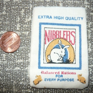 May include: A white fabric bag with the words "Extra High Quality" and "Nibblers" printed on it. The bag also features a cartoon rabbit and the text "Balanced Rations for Every Purpose".