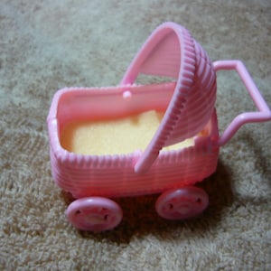May include: A pink plastic doll stroller with a wicker-like design and a white fabric lining. The stroller has a handle and a canopy.