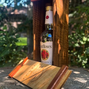 May include: A wooden box with a bottle of Four Roses Bourbon inside. The box is made of dark brown wood and has a rustic appearance. A wooden serving tray with the text "CCVFC" and "NORTH OF NORTHWEST" is in front of the box.