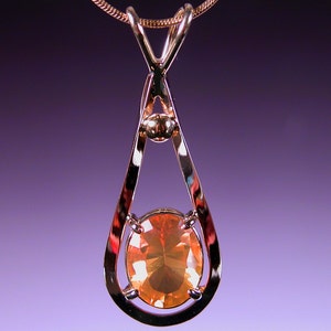 May include: A gold pendant necklace with a teardrop-shaped setting featuring a large, oval-shaped orange gemstone.