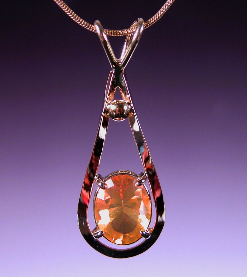 May include: A gold pendant necklace with a teardrop-shaped setting featuring a large, oval-shaped orange gemstone.