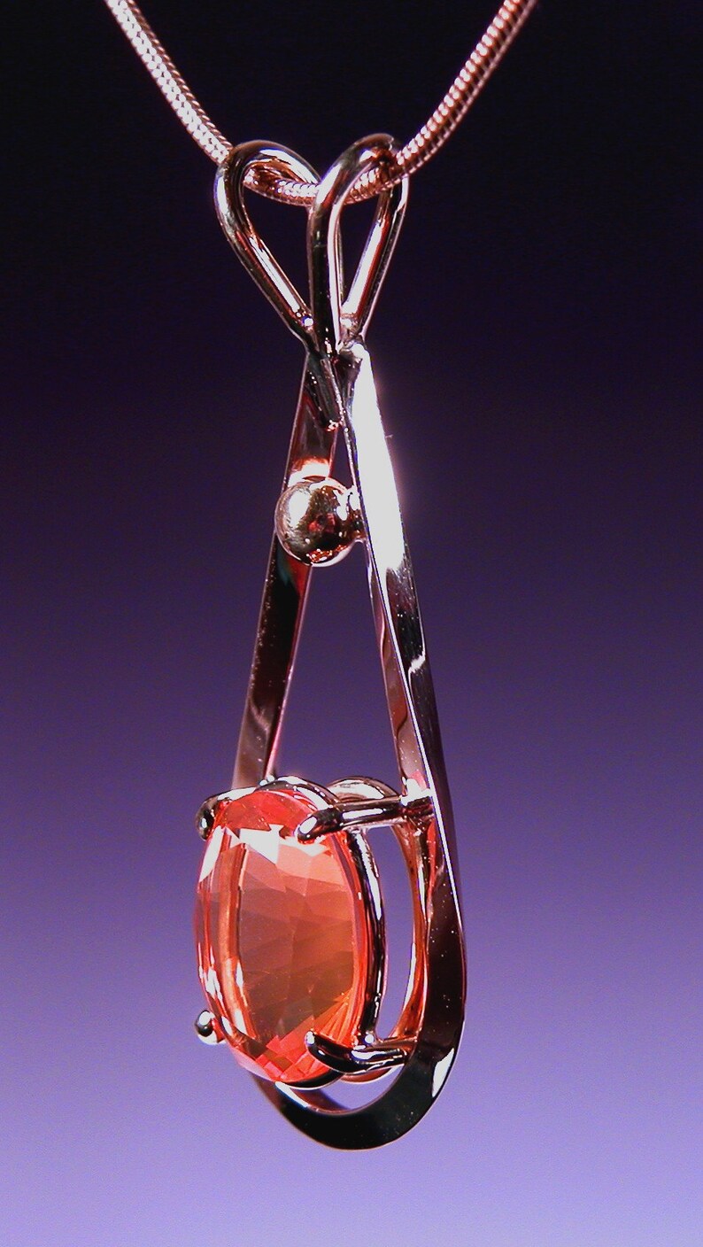 May include: A delicate gold pendant necklace with a heart-shaped bail and a large oval-shaped orange gemstone.