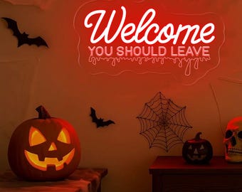 May include: A Halloween-themed scene with a glowing red neon sign that reads "Welcome YOU SHOULD LEAVE." The image includes a carved pumpkin, bats, a spiderweb, a small pumpkin, and a skull. The scene is lit with a red glow.