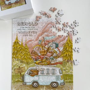 Op de afbeelding: Een gedeeltelijk gemonteerde legpuzzel met een illustratie van een lichtblauwe bus volgepakt met bagage en een fiets. De puzzel bevat de tekst "BEHOLD I AM WITH YOU AND WILL KEEP YOU WHEREVER YOU GO".