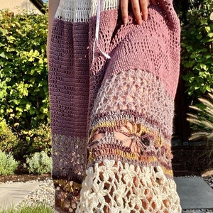 Peut inclure: Une longue jupe en crochet avec un motif multicolore. La jupe est faite de différents points et textures, et présente une bordure en crochet blanc en bas.
