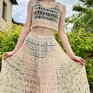 Puede incluir: Un conjunto de top y falda de crochet de color crema. El top es un estilo de tanque recortado con un escote amplio y abierto. La falda es un estilo largo y fluido en forma de A con una cintura de cordón.