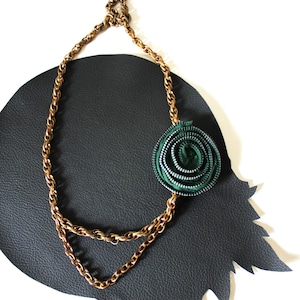 Puede incluir: Un collar de cadena dorada con un colgante de flor de cremallera verde.