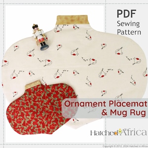 May include: A cream-colored placemat and mug rug set with a bird pattern, a red and green holly-patterned mug rug, and a toy soldier. The placemat has a gold-colored trim and the text "Ornament Placemat & Mug Rug".