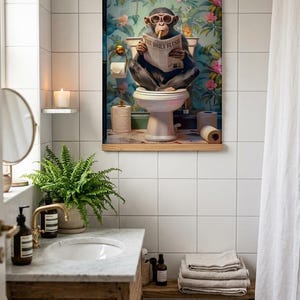 May include: A framed wall art print featuring a chimpanzee wearing pink glasses, sitting on a toilet, and reading a newspaper titled The Daily Flush. The background shows a vibrant floral wallpaper pattern with green leaves and pink flowers.