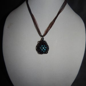 May include: A necklace with a brown ribbon and a black metal pendant with a turquoise center.