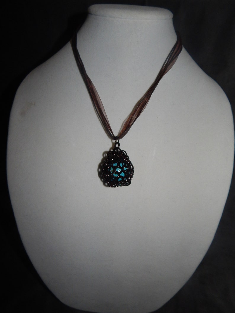 May include: A necklace with a brown ribbon and a black metal pendant with a turquoise center.