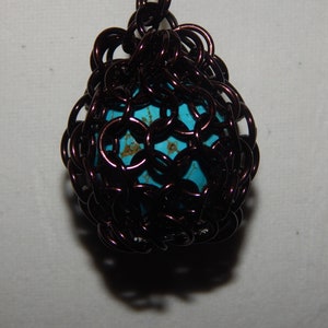 May include: A turquoise blue bead encased in a brown wire cage. The cage is made of small, interconnected loops of wire, creating a delicate and intricate design.