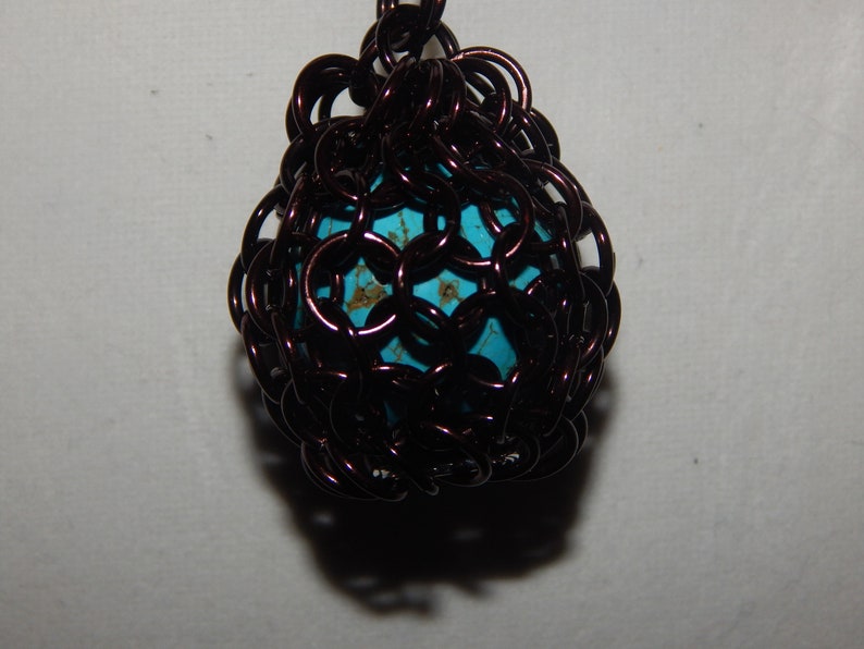 May include: A turquoise blue bead encased in a brown wire cage. The cage is made of small, interconnected loops of wire, creating a delicate and intricate design.