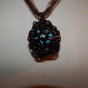 May include: A turquoise gemstone pendant encased in a brown wire cage, hanging from a brown ribbon.
