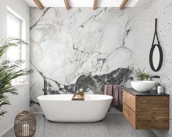 Puede incluir: Un baño moderno con una bañera ovalada blanca, un mueble de baño de madera con un lavabo blanco y un espejo con marco negro. Las paredes presentan un diseño de mármol y un patrón moteado. También se ven una linterna decorativa con velas y una planta en maceta.
