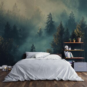 May include: A bedroom with a white bed and a wall mural of a foggy forest with tall trees. The mural is a dark green and blue color with a light yellow fog. There is a small shelf with books and a skull on it.