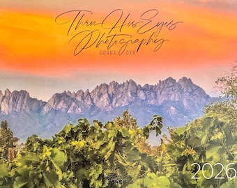 May include: A calendar featuring a scenic landscape with mountains, lush green foliage, and a vibrant orange and yellow sky. The text "Thru His Eyes Photography" and "Donna Cyr" are displayed in elegant script. The year "2026" is visible at the bottom.
