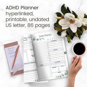 May include: A white and green daily planner with a section for daily goals, to-do list, and water intake. The planner is open to a page with a section for daily goals and a section for daily planning. The planner is on a white surface with a cup of coffee and a flower.