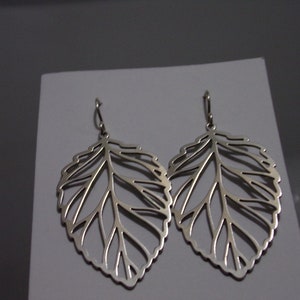 May include: A pair of silver leaf earrings. The earrings have a detailed, openwork design, replicating the veins and edges of a leaf. They hang from a simple hook.