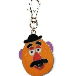 K&ouml;nnte beinhalten: Ein silberner Schl&uuml;sselanh&auml;nger mit einem Cartoon-Mr. Potato Head mit schwarzem Hut, orangefarbenem Gesicht, lila Ohren, roter Nase und schwarzem Schnurrbart.