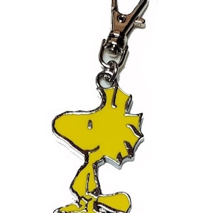 May include: A yellow metal keychain featuring a cartoon character, Snoopy, with a silver metal clasp.