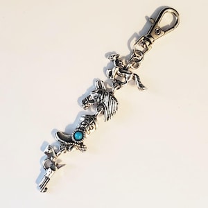 May include: Silver-toned keychain featuring Western-themed charms. The charms include a cowboy on a horse, a horse head, a cowboy boot with a turquoise stone, and a pistol. The keychain has a lobster clasp for easy attachment.