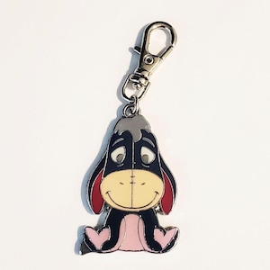 May include: A metal keychain featuring Eeyore from Winnie the Pooh. The charm is dark blue with a light yellow muzzle, pink feet and ears, and a silver clasp. The keychain is a cute accessory.