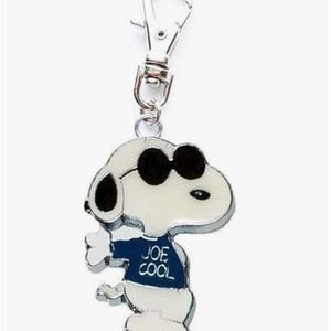 May include: A Snoopy keychain in a cool pose, wearing black sunglasses and a navy blue shirt with the words "JOE COOL". The keychain is white, black, and silver, with a lobster clasp for easy attachment.