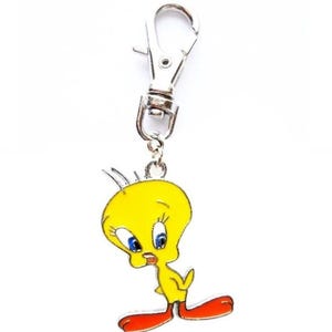 May include: A yellow Tweety Bird keychain charm with blue eyes and red feet. The charm is attached to a silver-colored metal clasp. The cartoon character is a classic design.
