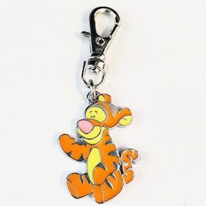 May include: A silver metal keychain featuring a cartoon image of the character Tigger from Winnie the Pooh. Tigger is orange and black with a yellow belly and pink nose.