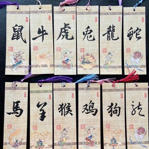 Puede incluir: Conjunto de doce marcapáginas rectangulares con caracteres e ilustraciones chinas. Cada marcapáginas presenta un animal del zodiaco diferente, con borlas de colores en la parte superior. Los caracteres están en tinta negra sobre fondo beige.