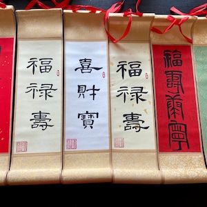 May include: Six traditional Chinese calligraphy scrolls with red and gold accents. The scrolls are mounted on wooden dowels and feature black ink calligraphy on white, red, and green paper. The calligraphy includes the characters "福" (fú), "壽" (shòu), "富" (fù), "貴" (guì), "康" (kāng), and "寧" (níng).