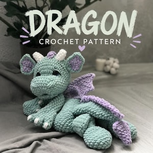 May include: A crocheted dragon in shades of teal and lavender, with white horns and claws. The text "DRAGON CROCHET PATTERN" is displayed above the dragon. The dragon is lying on a gray surface.