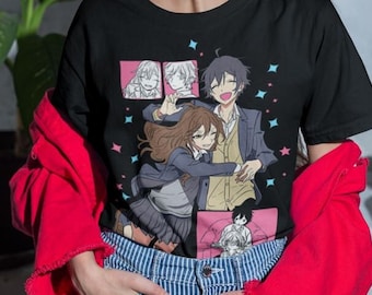 May include: A black t-shirt with a colorful anime graphic print featuring a group of characters. The graphic includes a couple hugging, a man with a guitar, and a man with a microphone. The shirt is worn by a person with long brown hair and a red jacket.