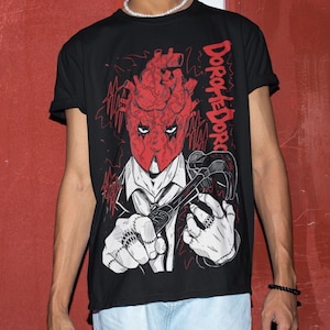May include: Black t-shirt with a graphic print of a red heart-shaped head with a menacing expression holding a wrench. The text "Dorothee Dorc" is printed on the shirt.