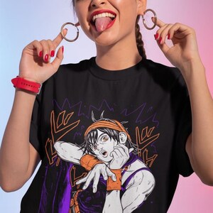Może przedstawiać: Czarny T-shirt z nadrukiem graficznym postaci z kresk&oacute;wki w pomarańczowych i fioletowych ubraniach. Postać wykonuje gest ręką i ma zaskoczony wyraz twarzy. Tekst "ORA ORA" jest nadrukowany na koszulce japońskimi znakami.