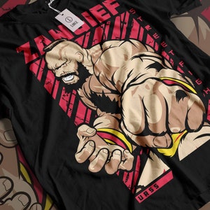 Könnte beinhalten: Schwarzes T-Shirt mit einer roten und gelben Grafik einer muskulösen Figur mit Bart. Die Grafik enthält den Text "ZANGIEF" und "STRENGTH" in Rot und "USSR" in Weiß.