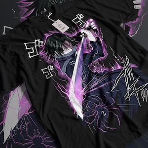 May include: Black t-shirt with a pink and white illustration of a character wielding a sword. The character has black hair and is wearing a black mask. The background features pink lightning bolts and the Japanese text "蜘蛛"