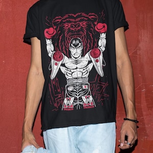 May include: Black t-shirt with a graphic print of a boxer with a bear behind him. The boxer is wearing boxing gloves and shorts with the text "Mamoru Takamura" on them.