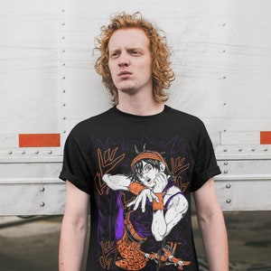 Może przedstawiać: Czarny T-shirt z nadrukiem graficznym postaci z kresk&oacute;wki w pomarańczowych i fioletowych ubraniach. Postać wykonuje gest ręką. Na koszulce widoczny jest napis "Giorno Giovanna".